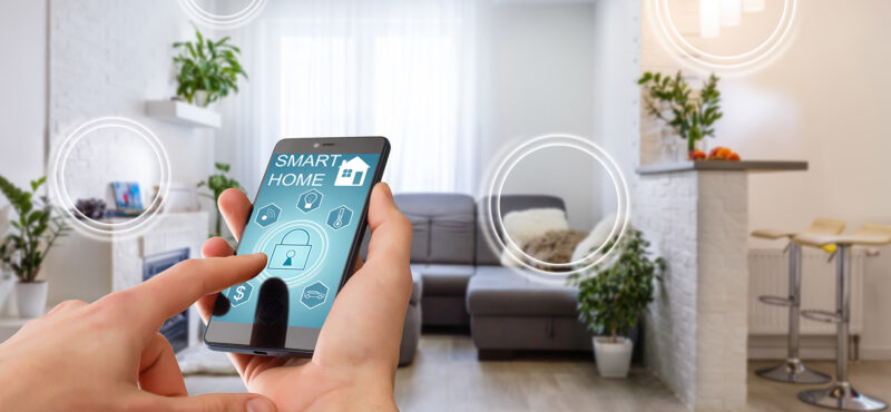 Smart home technology interface on smartphone app screen with augmented reality (AR) view of internet of things (IOT) connected objects in the apartment interior, person holding device